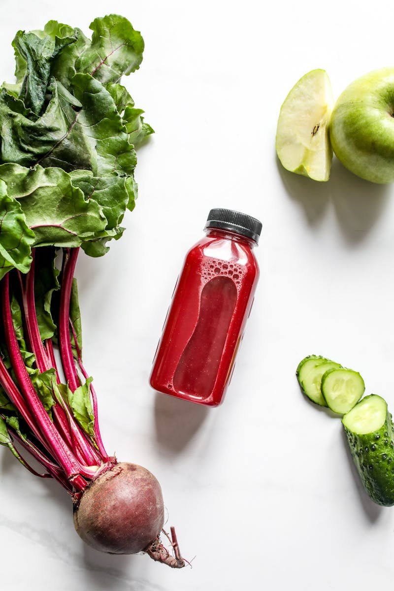 Top view of fresh beetroot, apple, cucumber, and juice bottle on a white background, showcasing healthy ingredients.